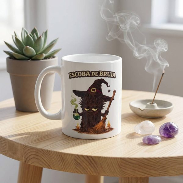 Taza de cerámica con ilustración de personaje Escoba de Bruja hecho de cianita negra con sombrero y escoba sobre mesa de madera con humo de incienso
