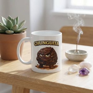 Taza de cerámica con ilustración de personaje Chunguita piedra shungit con cara enfadada sobre mesa de madera minimalista